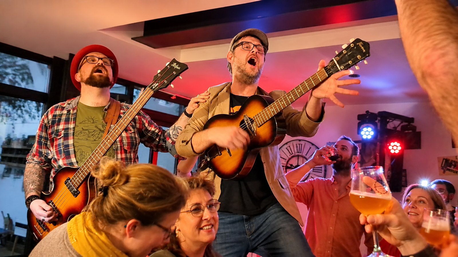 Concert à la Brasserie de Mai, deux musiciens guitare et basse au milieu du public, verres levés