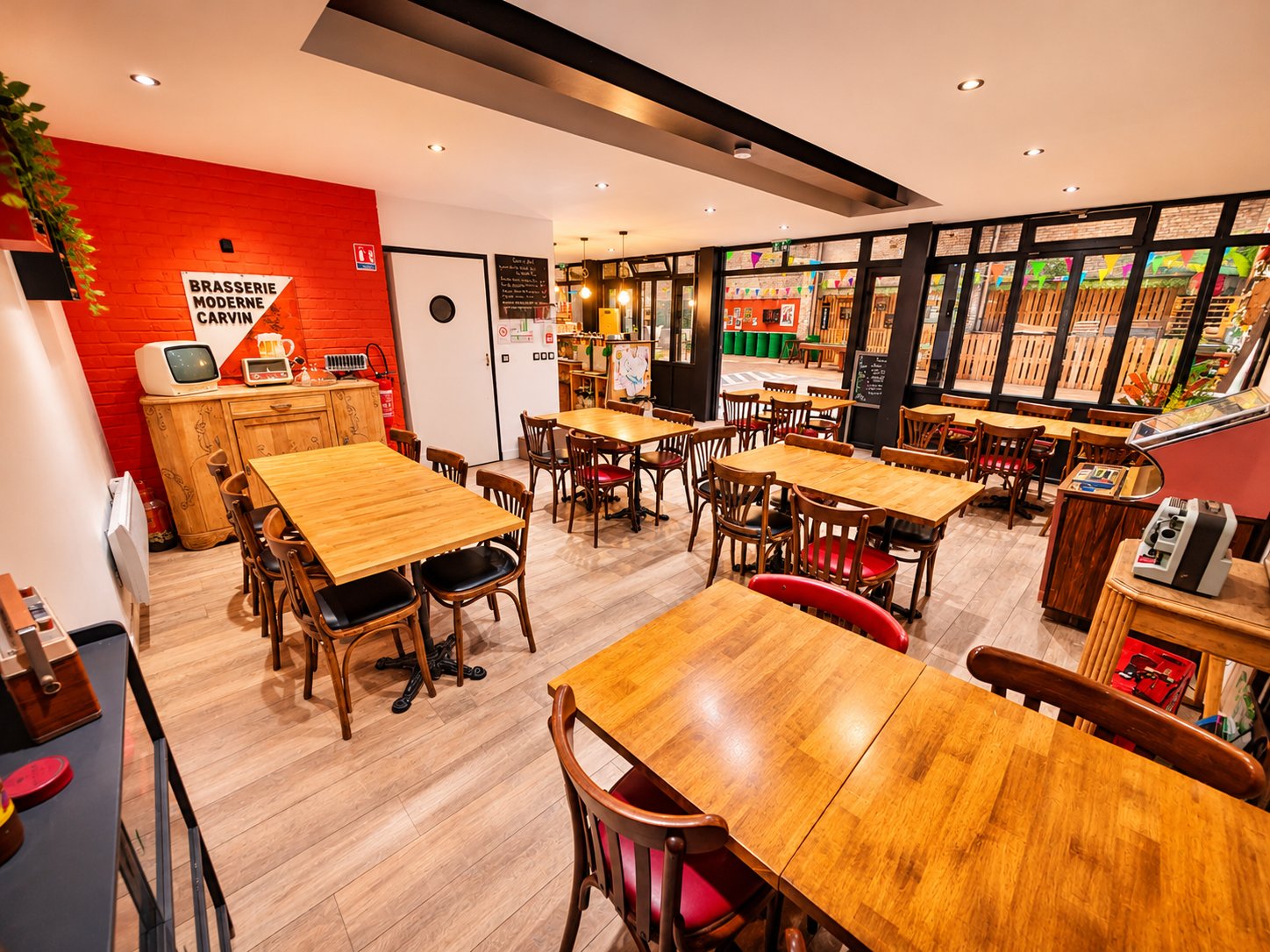 La salle de la Brasserie de Mai, tables en bois, chaises bistrot et mur de briques rouges